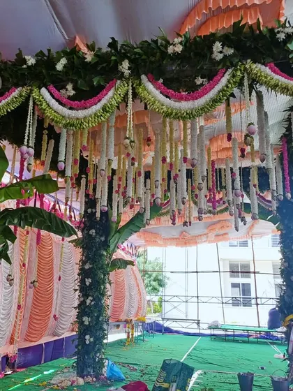 A view of a traditional mandap being set up under a large tent, with intricate floral work.