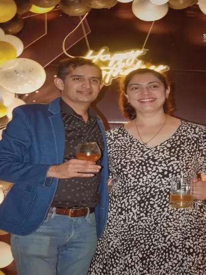 The happy couple at their birthday celebration, enjoying a drink against the backdrop of festive balloons.