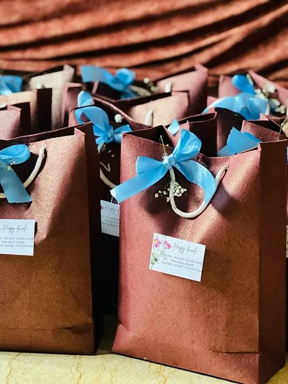 A large order of simple yet elegant brown paper bags, each decorated with a bright blue ribbon and a personalized 'Happy Diwali' tag.
