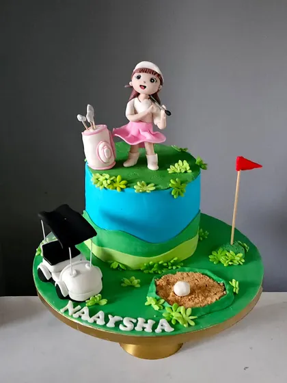 A special cake designed for a young golfer. The scene includes a handcrafted figurine of the birthday girl, a golf cart, and a sand bunker, all made from edible materials to create a fun and personalized sports-themed cake.