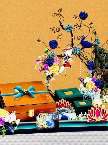 This Teej hamper is a work of art, featuring a decorative tree element and a peacock. The platter holds beautifully wrapped gift boxes, all brought together with a vibrant floral arrangement.
