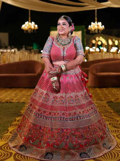 A full-length shot of a beautiful bride in her multi-colored lehenga, smiling brightly against the backdrop of her grand reception.