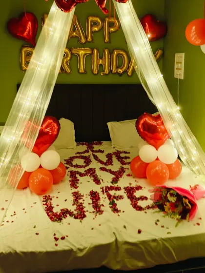 A birthday surprise for a wife. This romantic setup includes a fairy light canopy and 'LOVE MY WIFE' spelled out in rose petals on the bed.