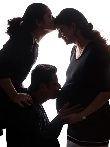 Welcoming a new baby is a moment for the whole family. This artistic silhouette maternity photo shows an older sibling and father sharing their love for the new arrival, creating a powerful family memory.