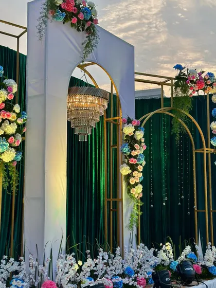 An elegant stage setup with gold-framed arches, a large chandelier, and emerald green drapes, perfect for a sophisticated wedding reception.
