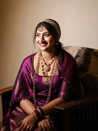 A seated portrait of a bride for her Oorkuduva. Her makeup is elegant, with a bold lip that complements her purple saree.
