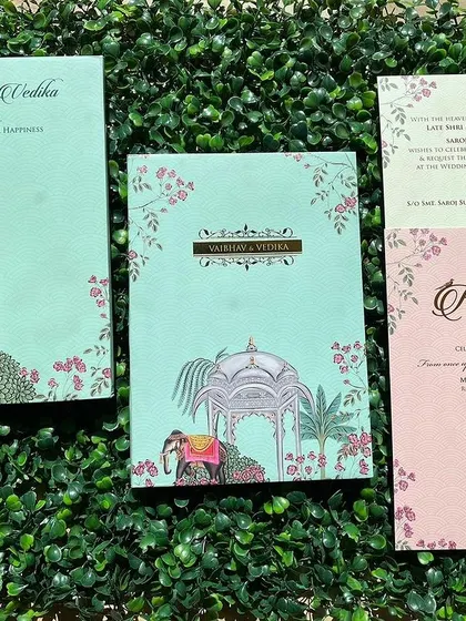 A complete invitation set with a pastel green and pink color scheme. The design features traditional motifs like elephants and gazebos within a modern botanical frame.