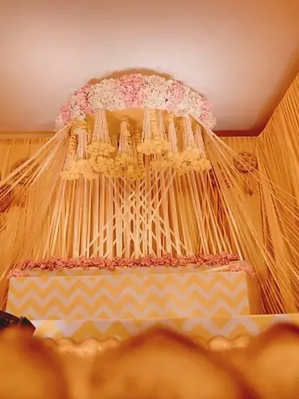 Here is the full view of the beautiful Haldi ceremony stage I designed. The setup features a canopy of hanging floral strings, a tiered seating area with a chevron pattern, and a large brass uruli in the front for the rituals.