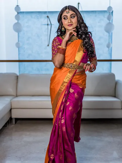 A full-length shot of a model in a vibrant orange and pink half-saree. This look is perfect for a pre-wedding event, featuring soft curls and dramatic eye makeup.