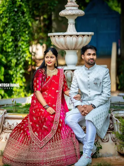 A beautifully composed portrait of a couple in traditional dress, posing elegantly by a garden fountain.