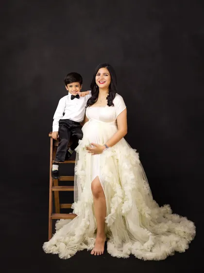 A lovely mother and son portrait during a maternity session. The mother's flowing white gown and her son's smart outfit create a beautiful contrast against the dark backdrop.