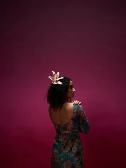 An artistic and moody shot for a clothing campaign. The makeup is minimal to suit the dramatic lighting, with a focus on the model's natural curly hair, accented with a fresh lily.