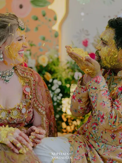 An adorable, playful moment between the couple during their Haldi ceremony, their faces covered in turmeric paste.