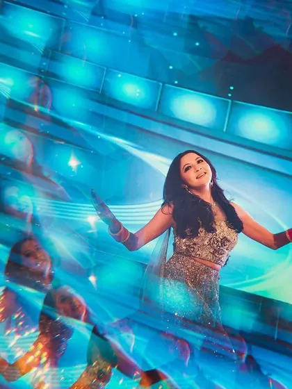 An artistic shot of the bride on the Sangeet dance floor. The use of motion blur and vibrant blue lighting creates a dynamic and energetic portrait that captures the spirit of the performance.