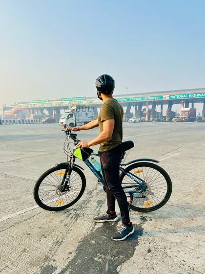 A solo moment of reflection for a rider after conquering a 100km milestone. Standing at the toll plaza, it's a reminder of the dedication it takes.