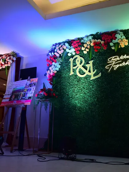 A photo booth for a Sangeet night with a lush green wall, floral decor, and neon signs.