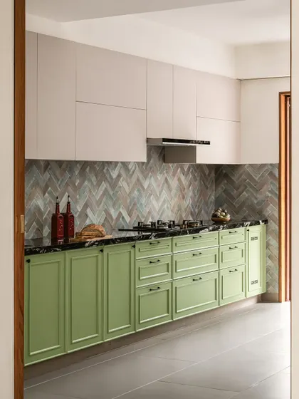 The kitchen in Kolam Pop, designed with The Kitchen Artisan, features classic shaker-style cabinets in a refreshing mint green, paired with a durable black granite countertop and a patterned tile backsplash.