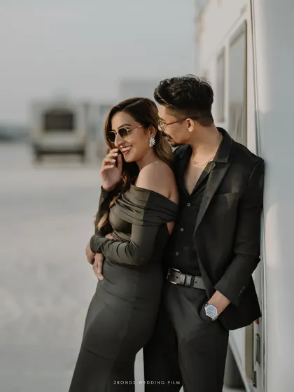 A candid moment of laughter and affection as the couple leans against a caravan in the desert, the golden hour light adding a warm glow.