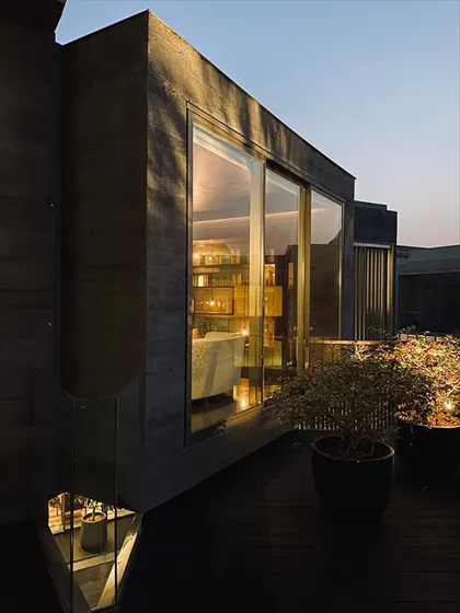 The warm interior light glows from a window of the Jenga House at dusk. This detail highlights the contrast between the solid concrete exterior and the life within the home.