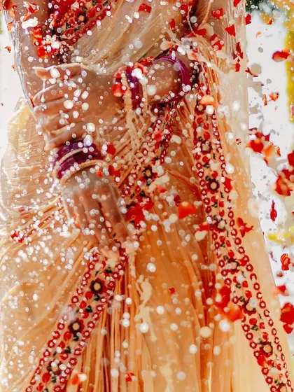 A close-up detail shot of the bride's attire being showered with water and petals. This artistic photo focuses on the textures, colors, and traditions of the Haldi.