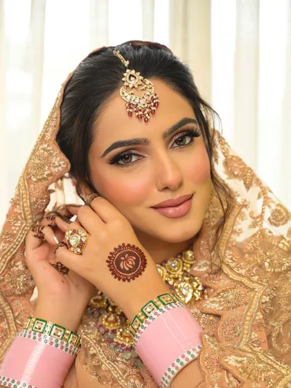 The intricate details of the henna and the traditional pink choora (bangles) are beautifully complemented by the soft, neutral makeup tones.