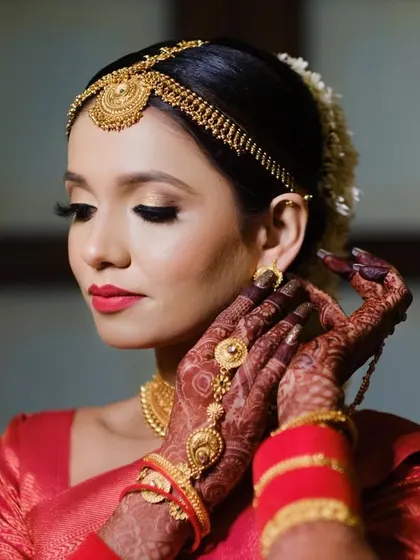 A stunning close-up of the bride, highlighting her traditional gold jewellery, red lipstick, and intricate mehndi. This is a classic bridal portrait that showcases her elegance.
