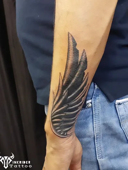 After: The finished wing tattoo features deep black shading and detailed feather textures. This powerful design not only covers the old script but also creates a dynamic and impressive piece of art.