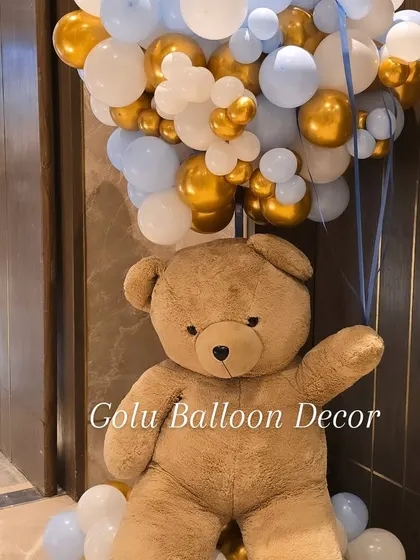 A close-up of a life-sized teddy bear holding a large bunch of balloons, a perfect welcoming prop for any celebration.