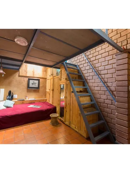 A cozy bedroom in the Sans Souci Residence featuring a mezzanine level to maximize space. The tall volume enhances cross-ventilation, and the use of natural materials like wood and earth creates a warm, healthy living environment.