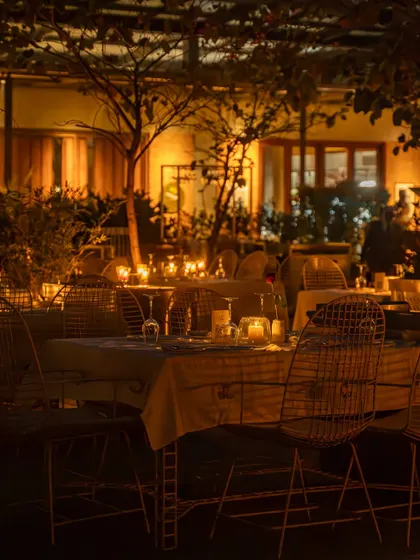 A view of the restaurant's candlelit tables through the trees. This perspective creates a sense of discovery and enchantment, highlighting the unique setting of the venue.