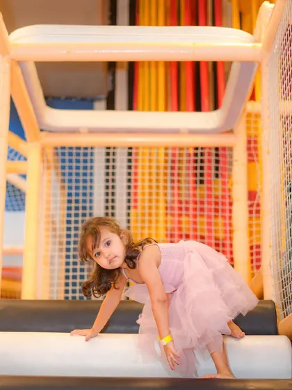 A little girl in a beautiful pink dress explores the climbing structure on her way to the slide.