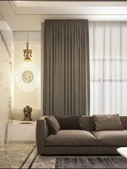This living room corner beautifully integrates a pooja space. The design uses a marble feature wall and a hanging 'Om' mandala to create a serene spiritual nook within the main living area.