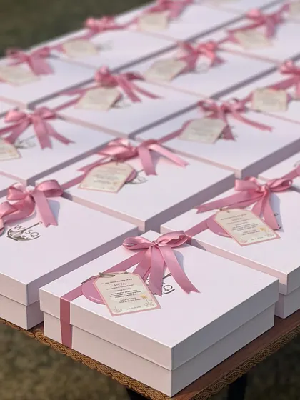 An array of our white gift boxes with pink ribbons and custom tags, prepared for a first birthday party. The uniform look creates a stunning display for large events.