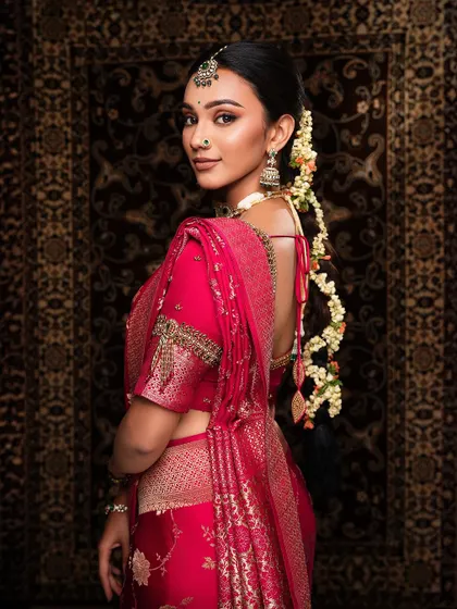 A beautiful back shot of a bride in a pink silk saree, highlighting the traditional hairstyle and the intricate design of the blouse.