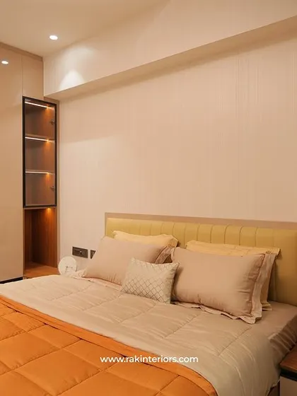 A bright and modern bedroom with an orange bedspread and a large wardrobe with sleek, handleless doors. A built-in vanity mirror and desk make the space highly functional.