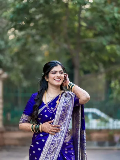 A candid shot of a bride in a stunning royal blue Paithani saree, sharing a happy, natural smile. We capture these unposed moments that truly reflect the joy of the day.