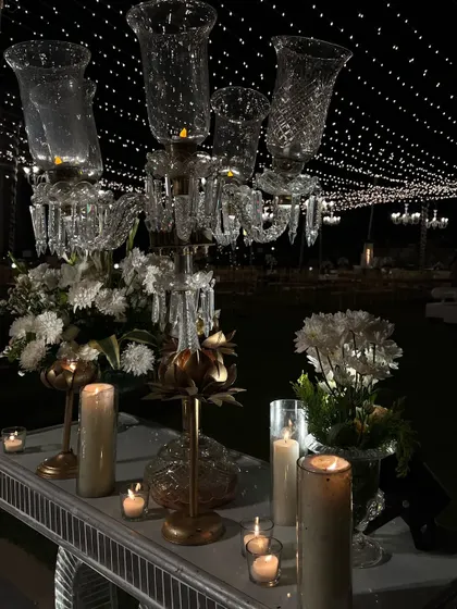 Details from a 'Heeramandi' aesthetic decor, featuring a crystal candelabra and white florals under a sky of fairy lights.