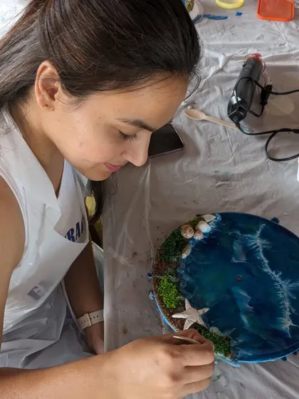 A participant carefully placing a starfish onto her resin beach clock, adding the perfect finishing touch to her creation.