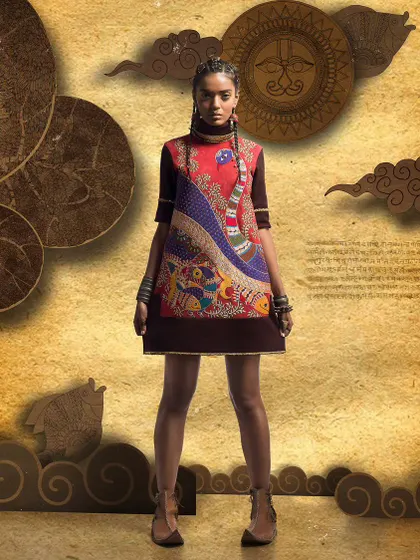 Full-length shot of a model in a short, art-inspired dress. The direct, centered pose against a textured, illustrative background makes the garment's unique peacock motif the central focus.