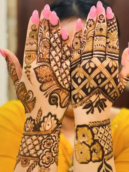 A modern take on bridal mehndi with two different designs on each hand. One features a peacock and floral vines, while the other uses a bold, diagonal checkered pattern.