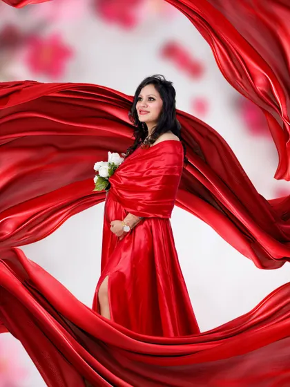 A glamorous studio portrait featuring a mother-to-be in a flowing red satin gown. The fabric swirls around her, creating a dynamic and artistic effect.
