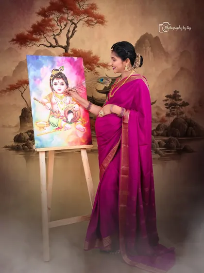 An expectant mother dressed in a beautiful pink saree adds the final touches to a painting of Little Krishna. This creative concept, set against a traditional painted backdrop in our studio, connects the mother's love to a divine theme.
