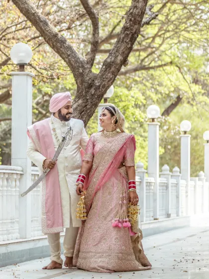 A full-length portrait of a smiling Sikh couple in their wedding attire, capturing a happy and relaxed moment on their special day.