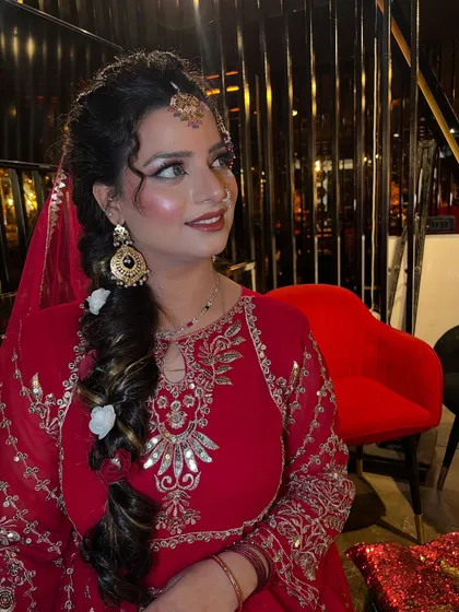 A beautiful portrait capturing a moment of reflection. The makeup looks soft and luminous, with a focus on the eyes and the traditional maang tikka that adorns her forehead.