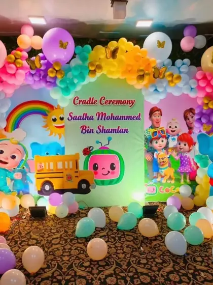 A Cocomelon themed cradle ceremony with a colorful backdrop and balloon arch.