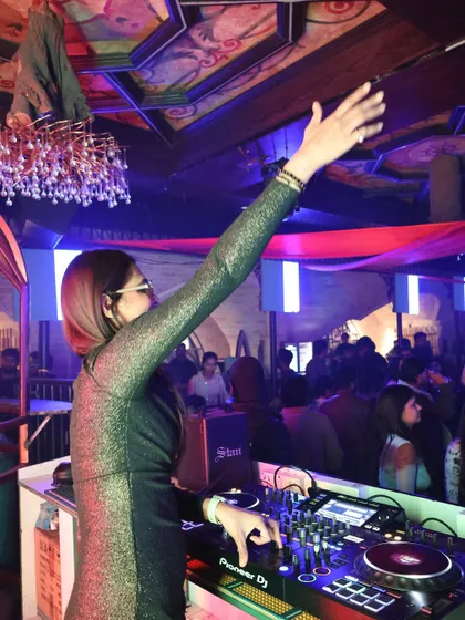 A classic DJ pose with one hand up, connecting with the crowd at Romeo Lane. This gesture unites the room and signals a big moment in the music.