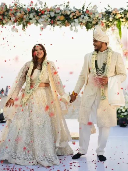 A full-length shot of the couple, hand in hand. The bride's minimal and radiant makeup look is perfect for her elegant ivory lehenga.