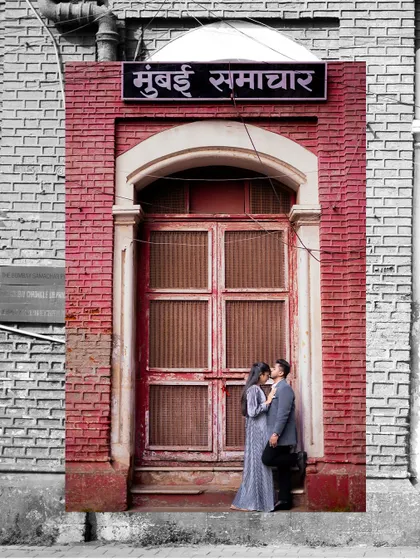 An artistic pre-wedding photo using selective color, highlighting the iconic red brick of a Mumbai Samachar building while the couple remains in a romantic embrace.