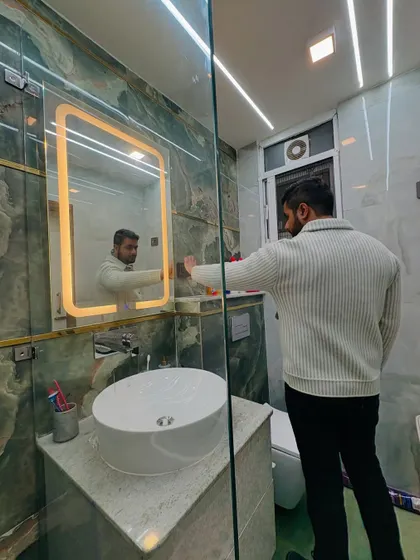 Here I am inspecting the backlit mirror in a newly renovated bathroom. The green onyx-style tiles and the modern vessel sink create a very high-end and stylish look.