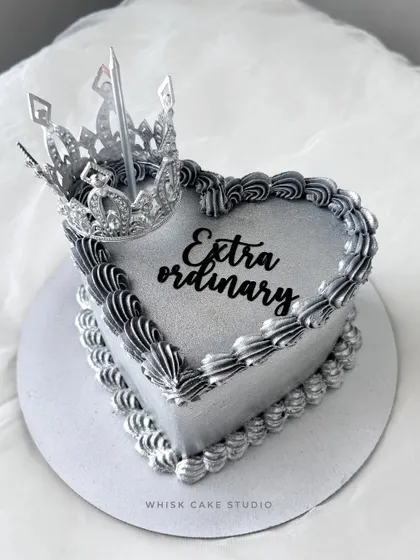 The silver glitter cake. This heart-shaped cake is all about sparkle, with a silver finish, black piping, and a crown topper that says "Extraordinary."